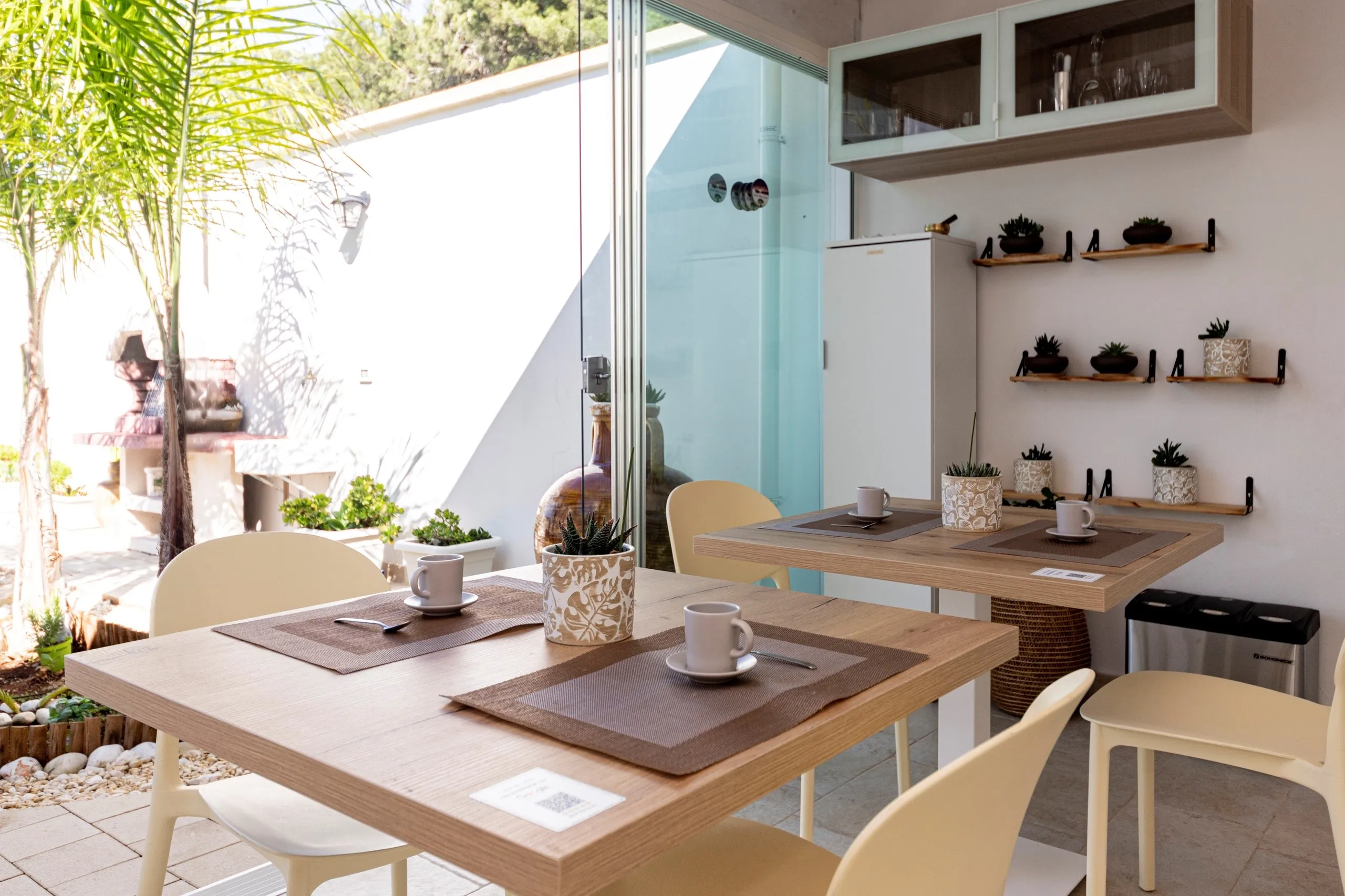 Une table dressée pour le petit-déjeuner, devant la baie vitrée donnant sur le jardin