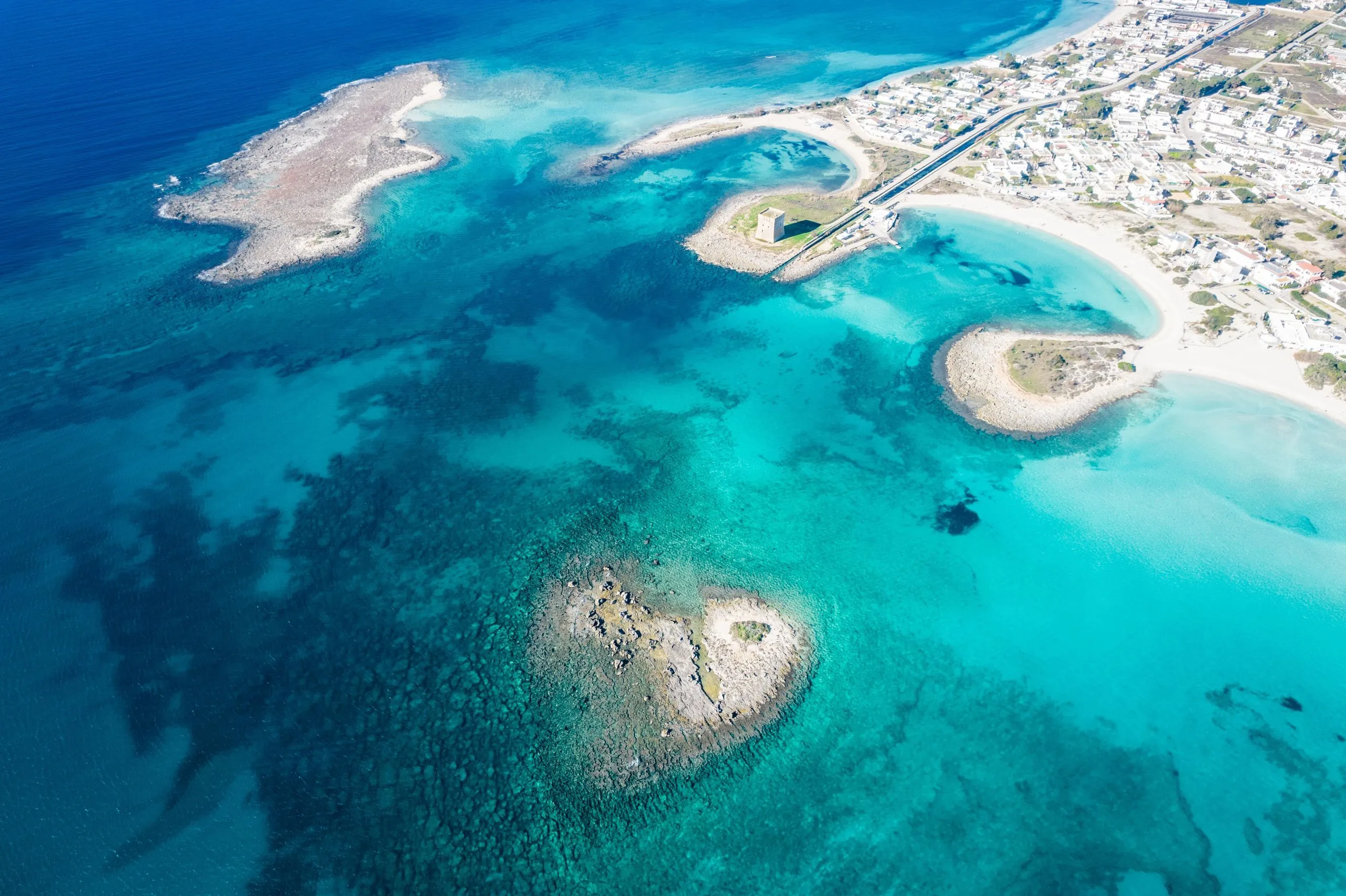 Porto Cesareo vista dall’alto: il mare turchese, gli isolotti bassi, la torre sull’isolotto col ponticello e il paese lungo la costa