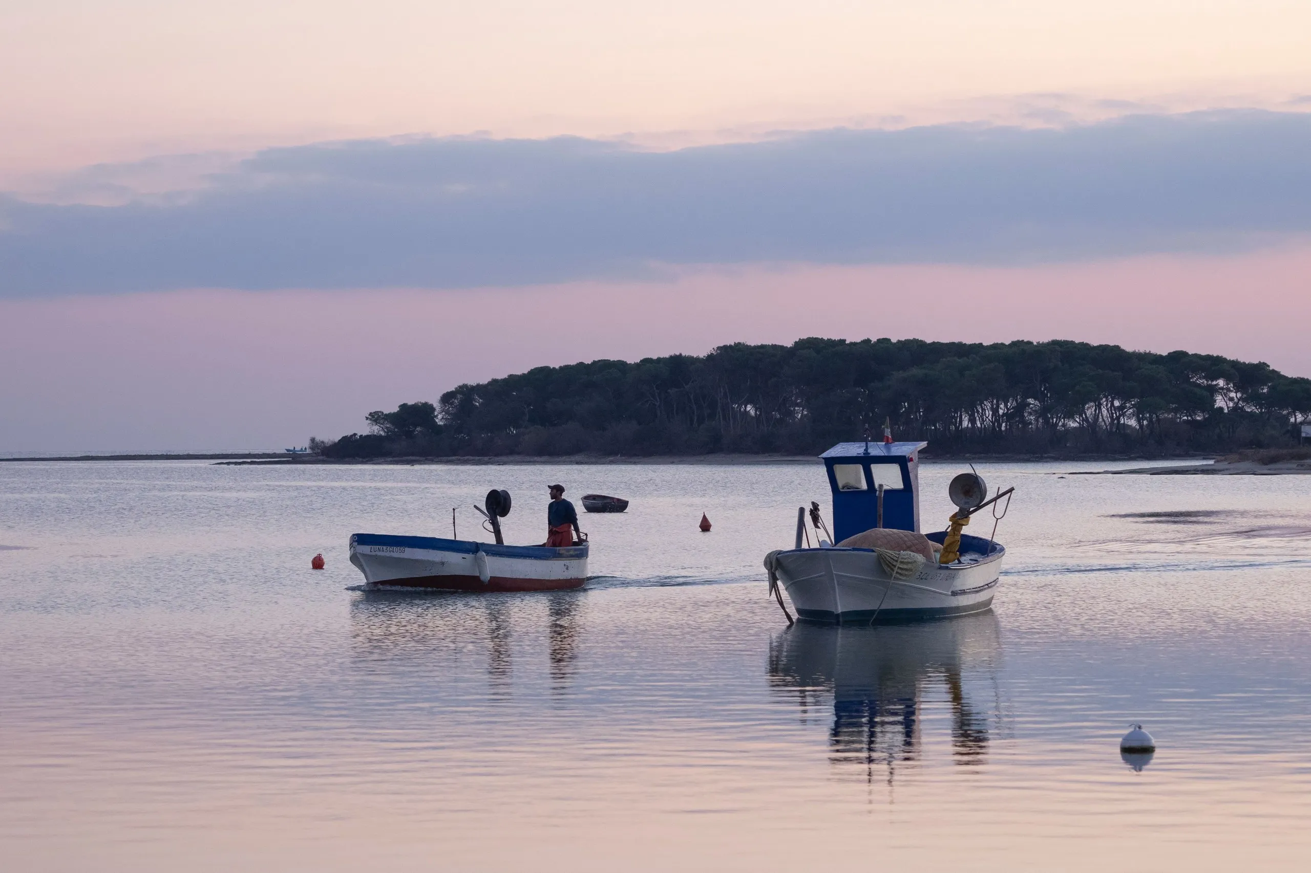 Due barche da pesca su acqua calma a luce rosata, con un isolotto alberato sul fondo